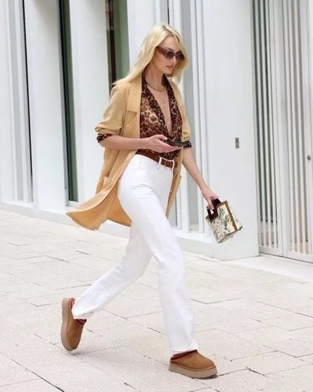 Woman wearing Ugg Ansley moccasin slippers with a striped Breton top and white jeans