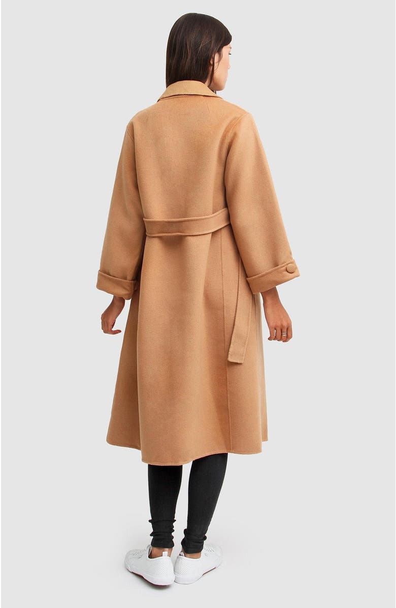 Back view of a woman in a belted camel wool coat, black leggings and white sneakers