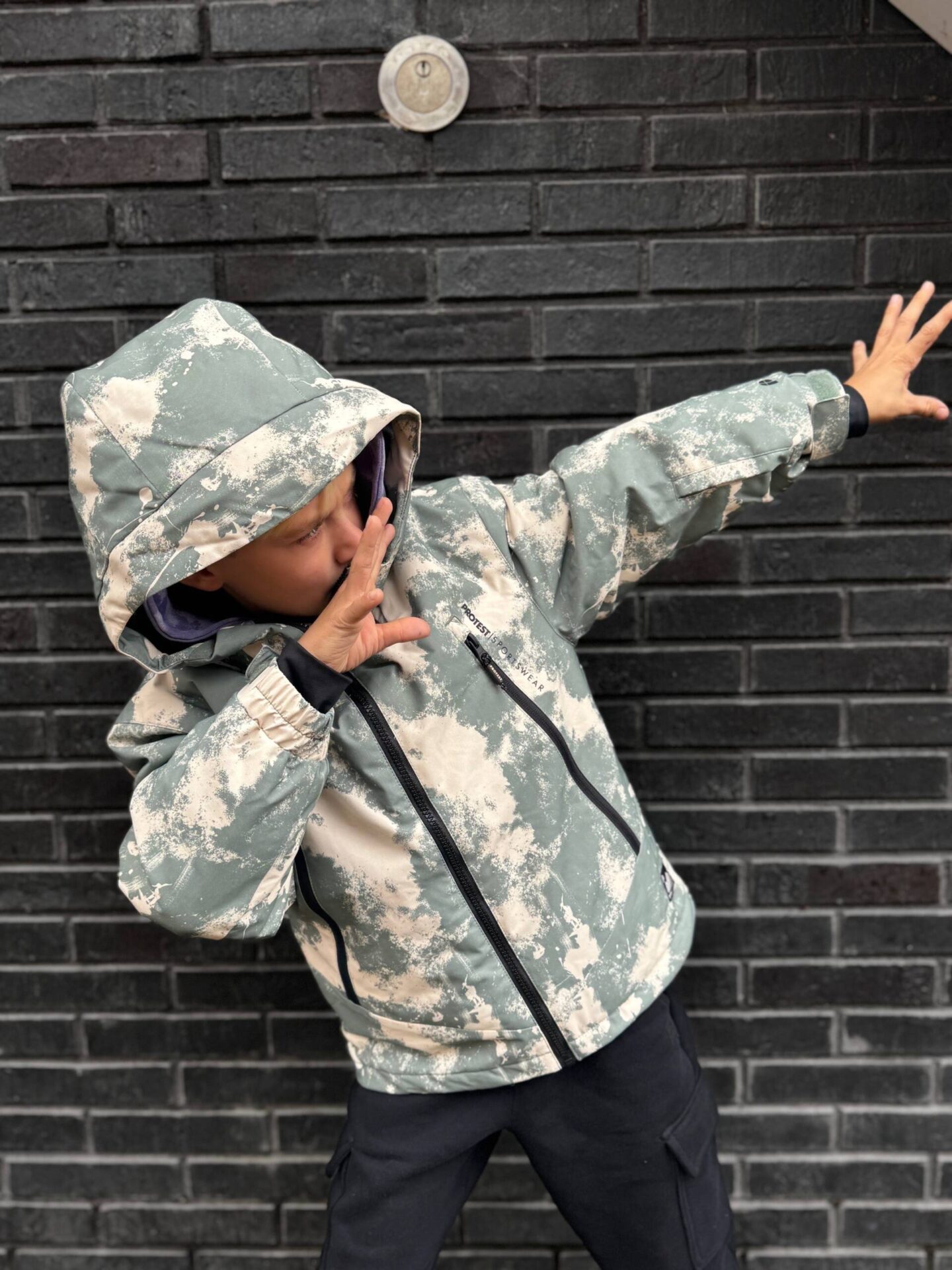 A boy wearing a camo-print hooded winter jacket with dark pants