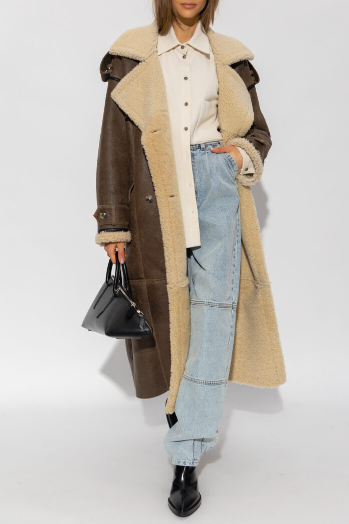 Woman in a long brown shearling coat with a cream shirt and wide-leg jeans in a studio portrait