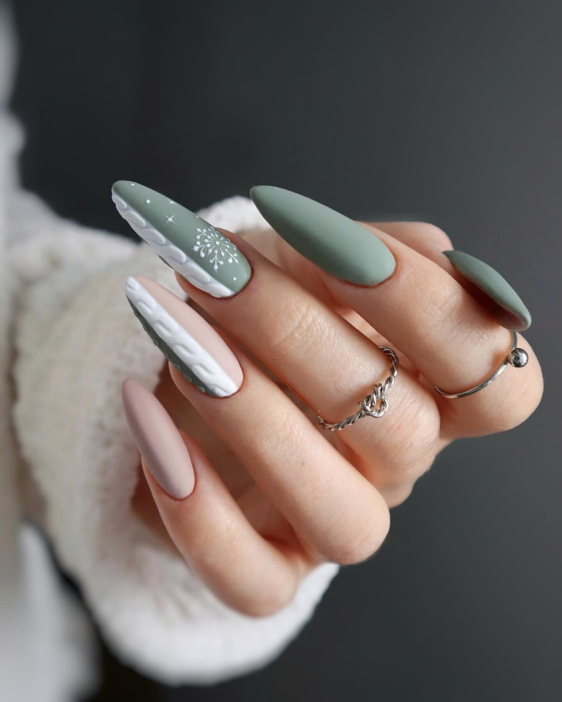 Matte sage green stiletto nails with white snowflake and dot accents and nude cable-knit nails