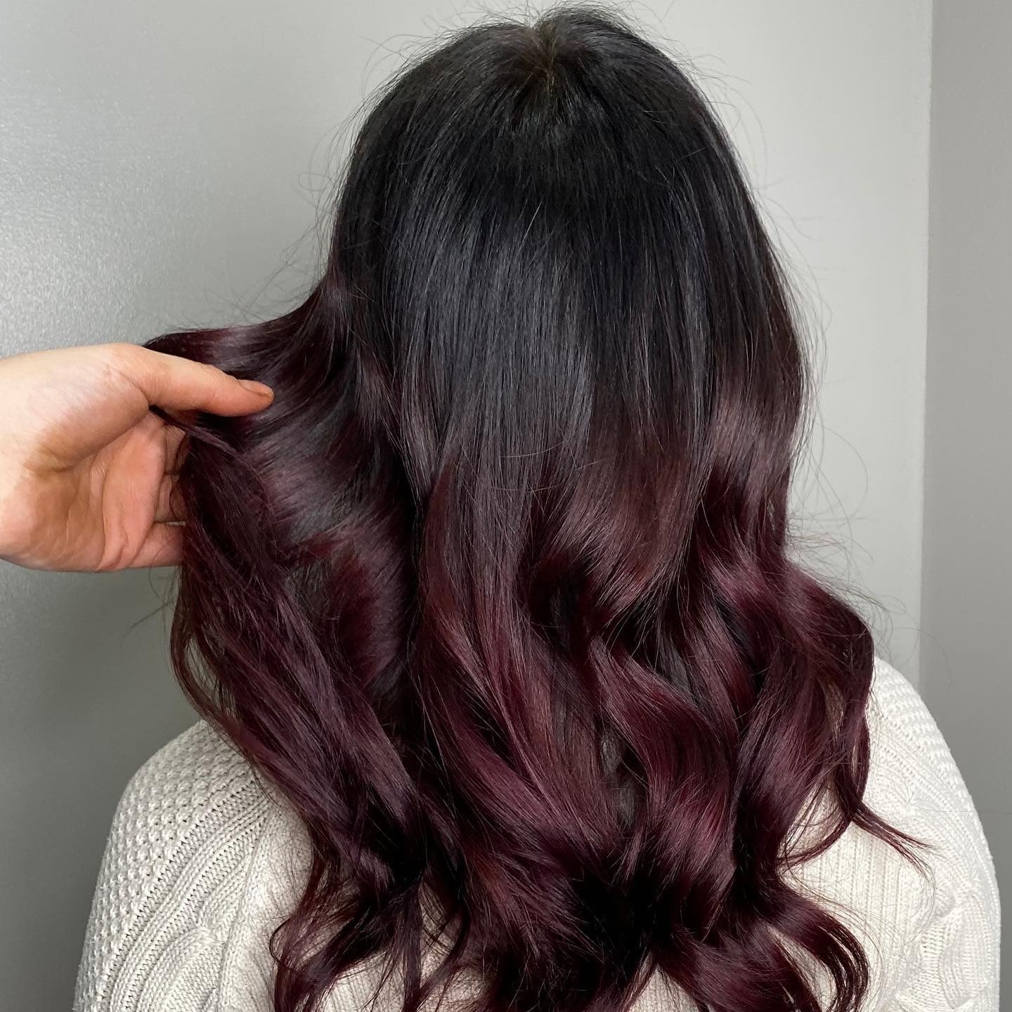 Back view of wavy hair with espresso-black roots blending into burgundy-plum sangria balayage ends