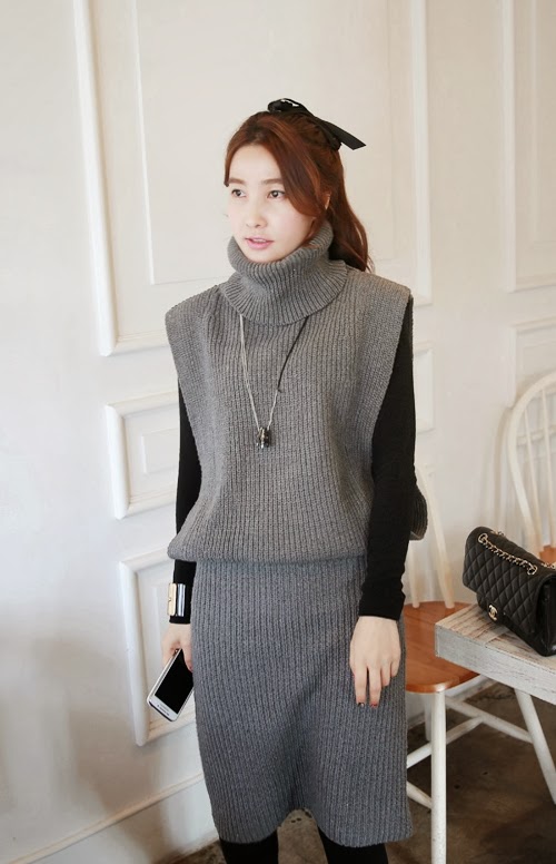 Grey ribbed-knit sleeveless pinafore dress layered over a black turtleneck with a long pendant necklace