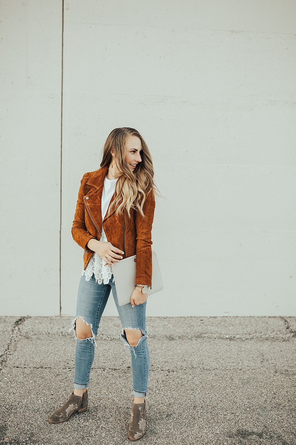 Woman in cognac suede moto jacket, white lace top and ripped jeans