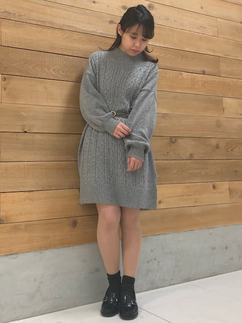 Grey cable-knit sweater dress cinched at the waist with a thin brown belt, black loafers and black socks
