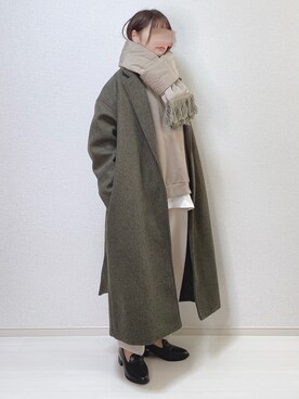 Person wearing an oversized sage green wool coat with a beige scarf and black loafers