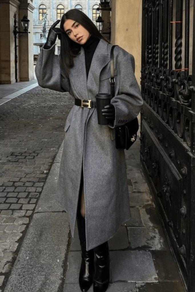 Woman wearing a black wrap coat over a grey turtleneck with black wide-leg trousers