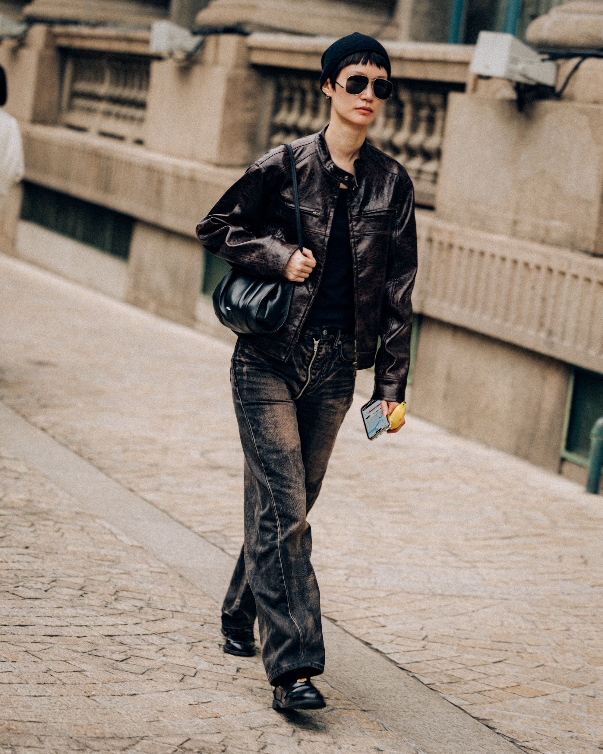 Woman in a black leather biker jacket, black top and dark wide-leg jeans with black loafers, a beanie and sunglasses
