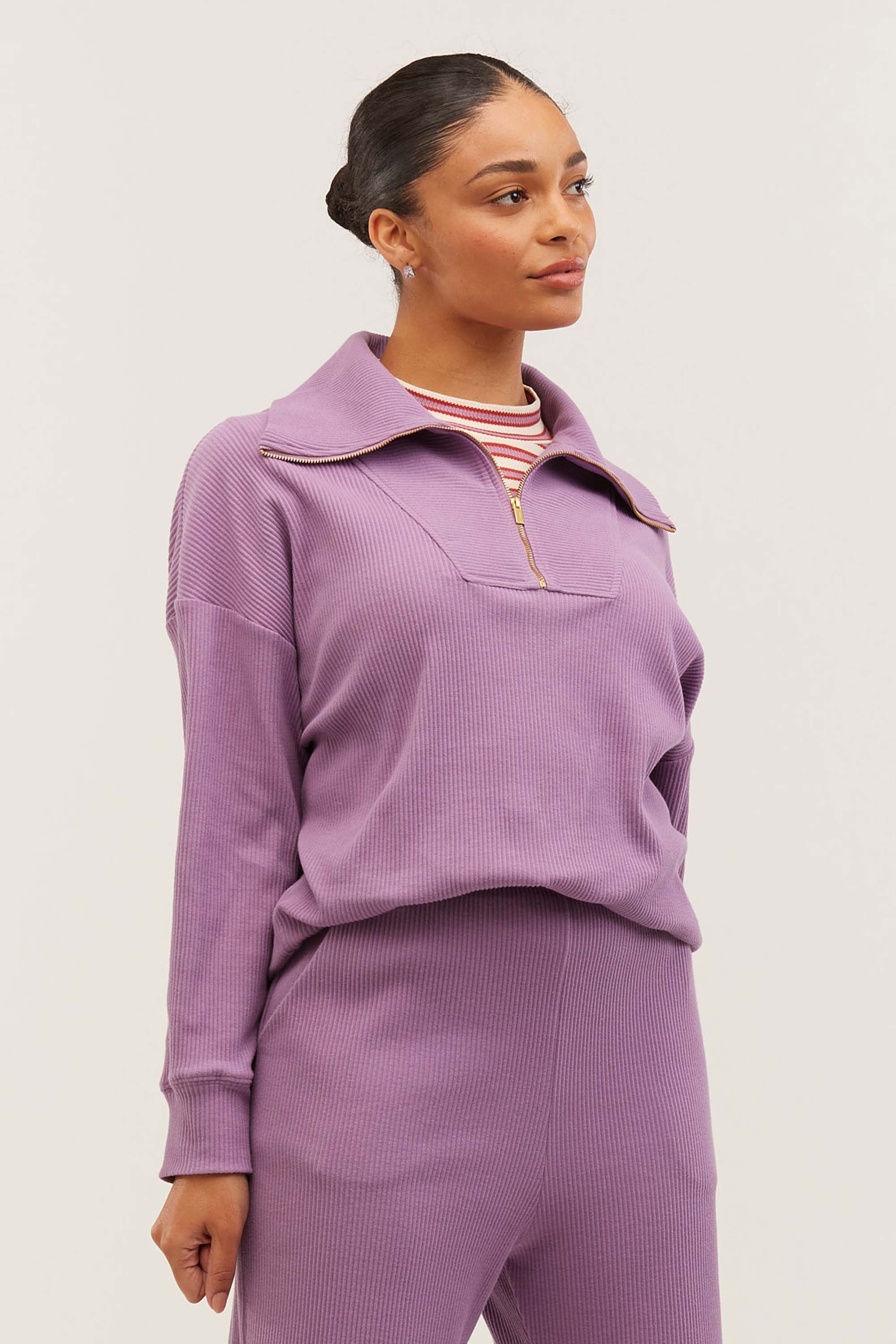 Woman wearing a lilac ribbed quarter-zip pullover with a striped tee underneath and matching ribbed pants