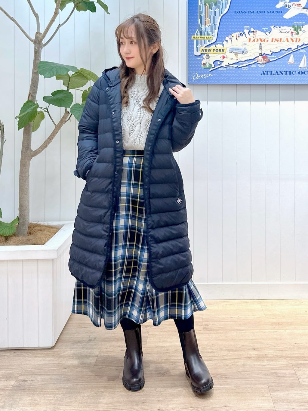A woman wearing a plaid long puffer coat with a cable-knit sweater and boots