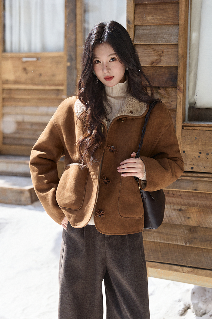 Woman wearing a caramel suede toggle jacket with shearling collar, cream turtleneck and brown trousers