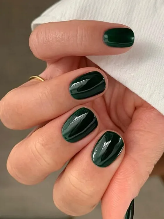 Short oval nails painted in glossy deep forest green