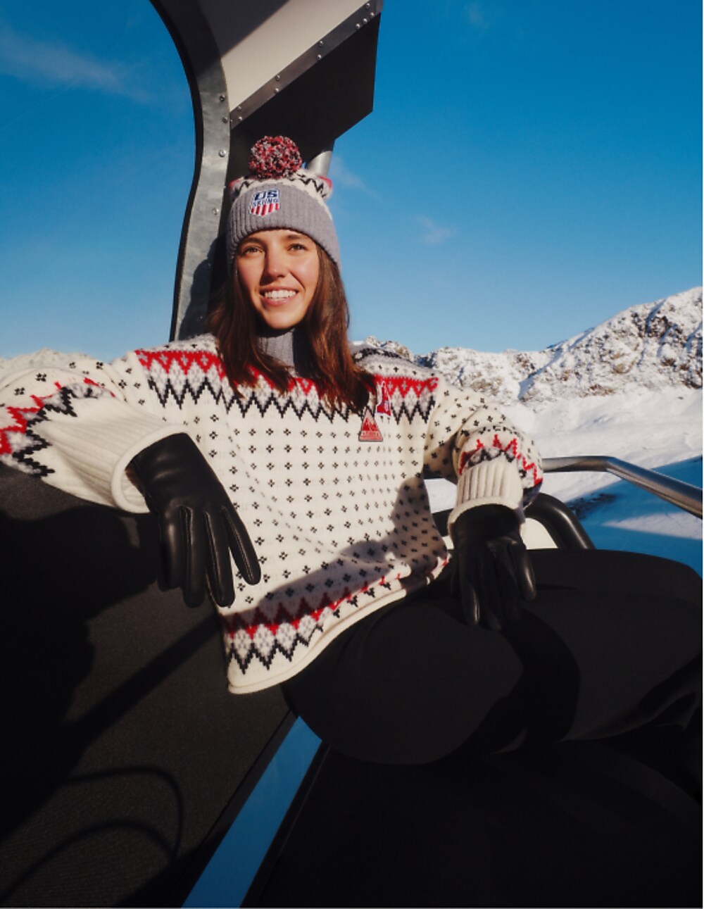 Woman in a white Fair Isle sweater with red and navy pattern, pom beanie and leather gloves on a gondola