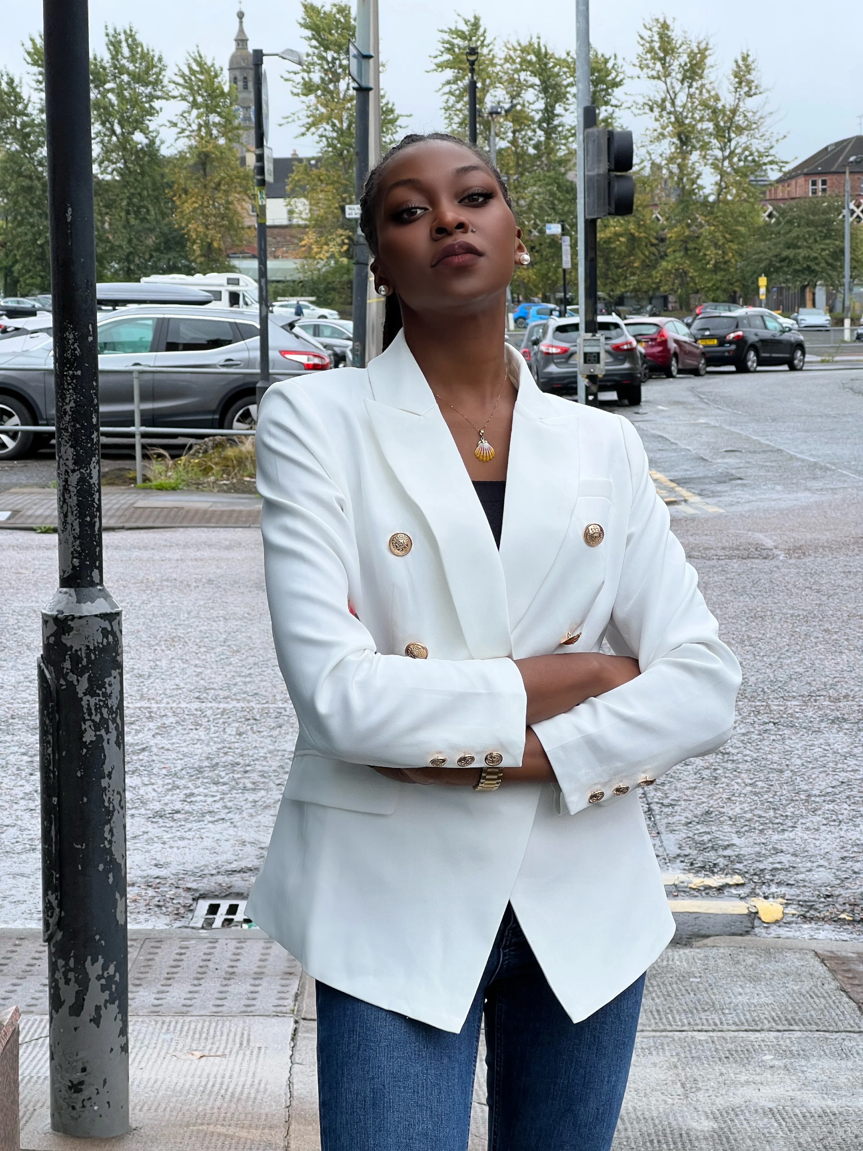 Woman on a city street wearing a white double-breasted blazer with gold buttons over a dark top and blue jeans