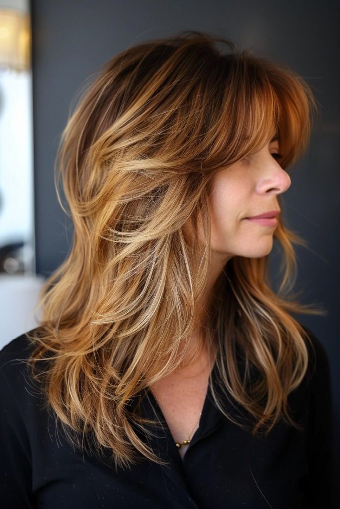Feathered mid-length layered haircut with curtain bangs and caramel highlights
