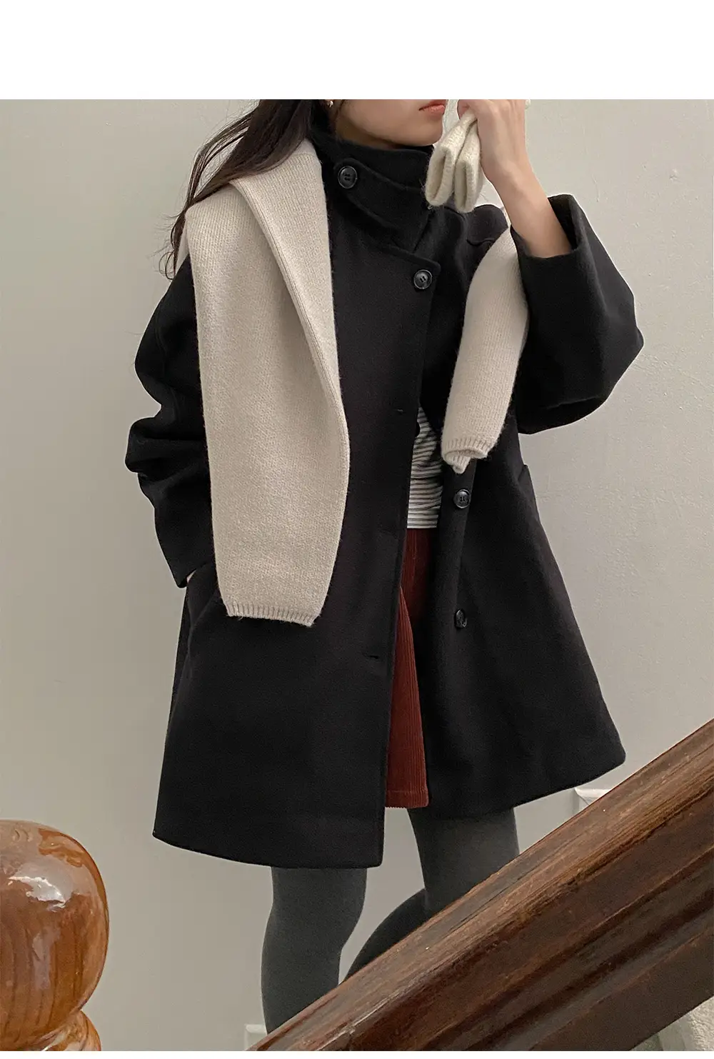 Woman in a black wool coat with a cream knit scarf draped over it and a rust corduroy skirt