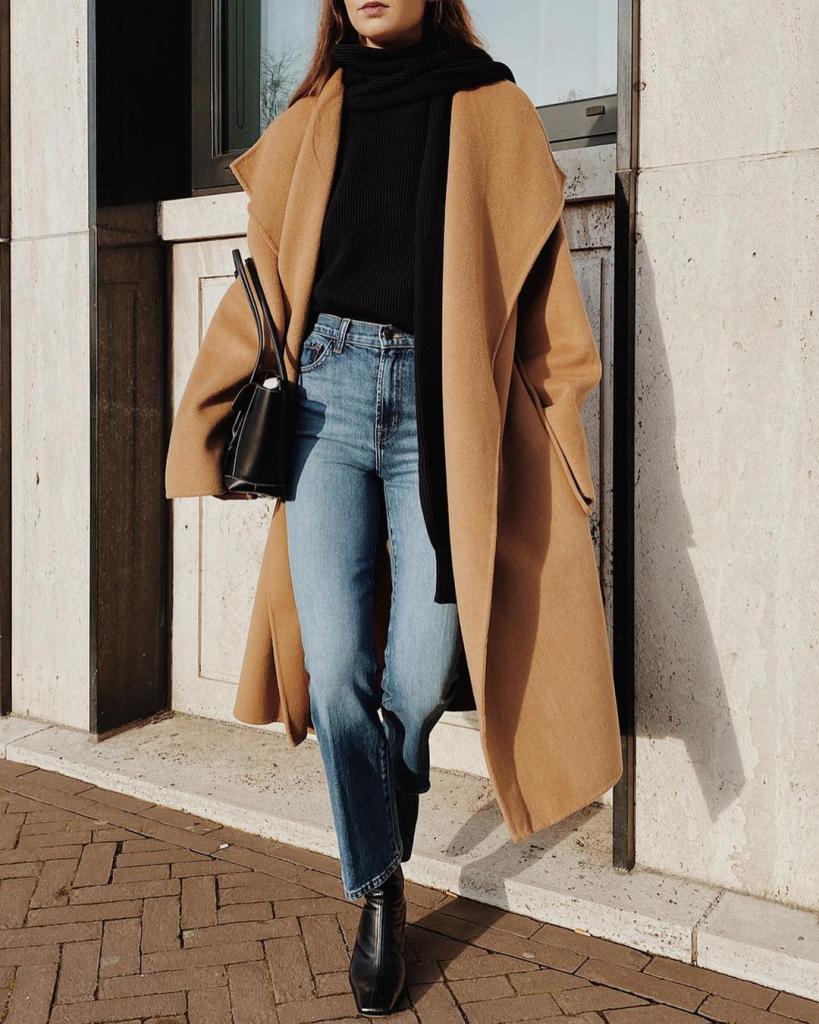 Woman wearing a black coat with a chunky cream scarf, jeans and boots