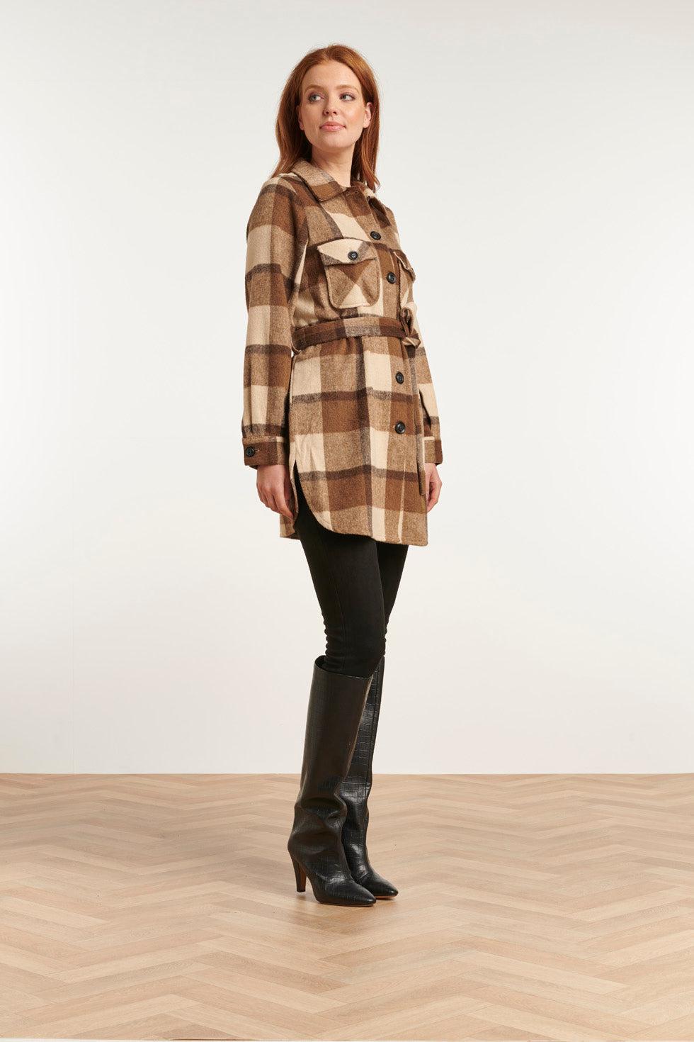 Woman in a brown buffalo-plaid belted shacket with black leggings and black croc-embossed knee-high boots