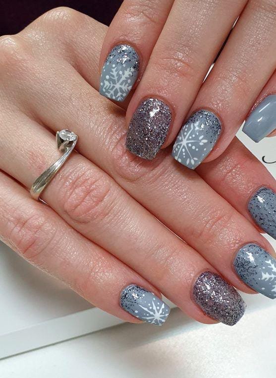 Soft gray nails with white snowflake designs and silver glitter
