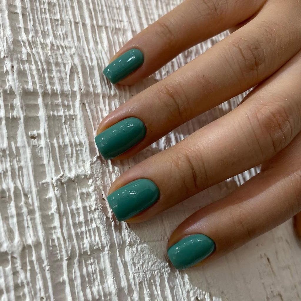 Short nails in deep teal green with a glossy finish