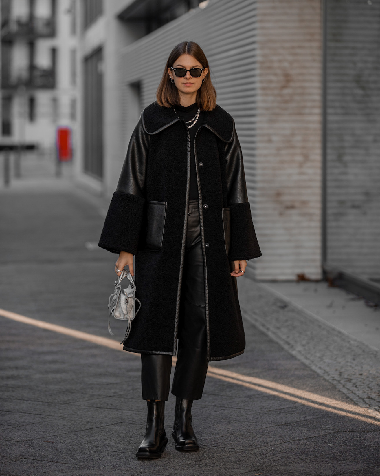 Woman in a black teddy coat with leather sleeves, black top, leather trousers and black boots