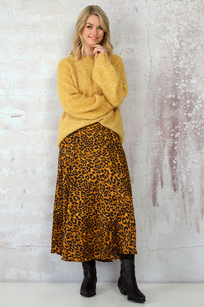 Woman in a mustard yellow knit sweater with a leopard print midi skirt and black boots