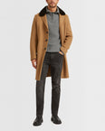 Man wearing a camel coat with a dark fur collar over a grey quarter-zip with chelsea boots