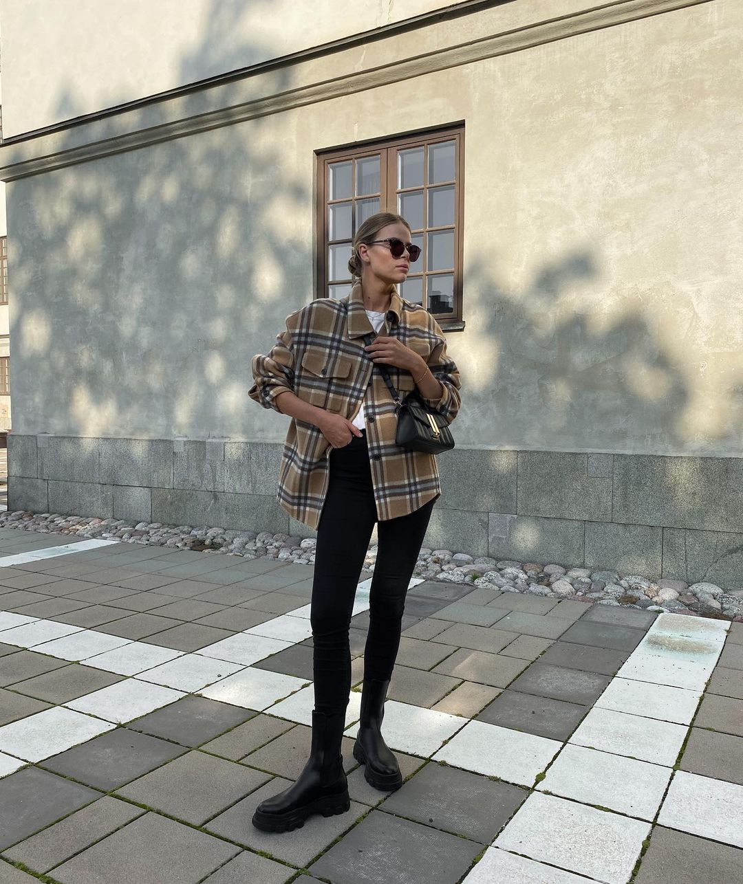 Woman in a tan plaid shacket with black skinny jeans and chunky black boots