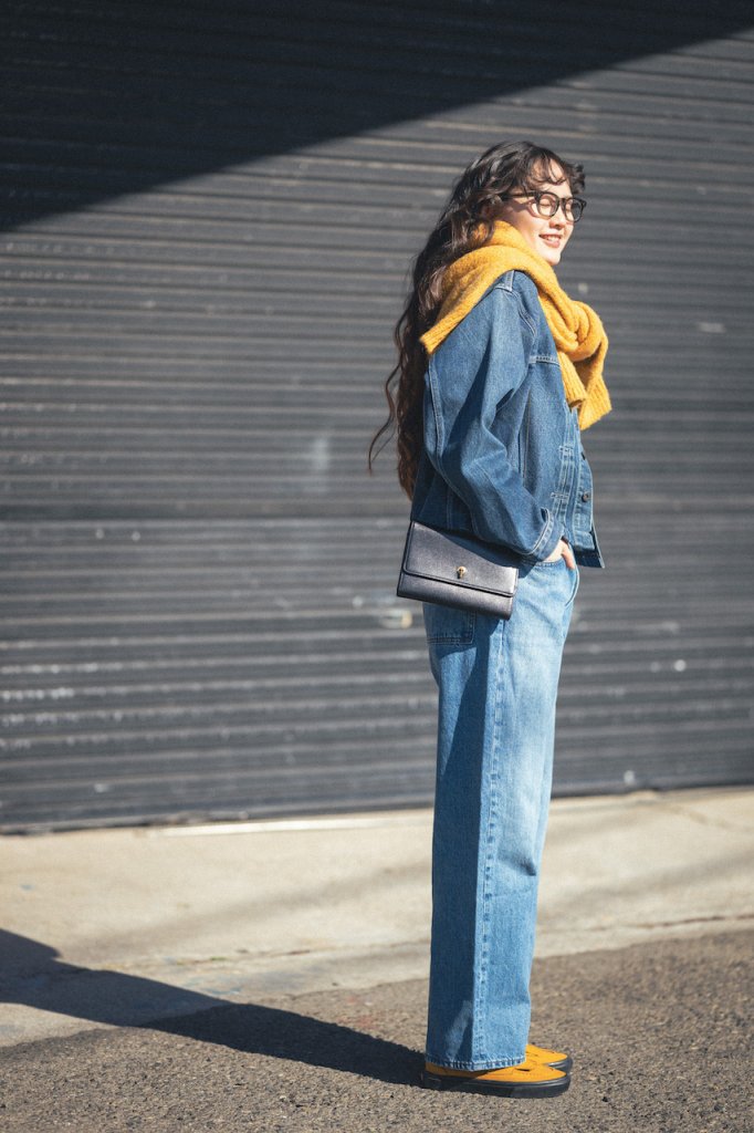 Woman with a mustard yellow scarf draped over her shoulders like a shawl, denim jacket and wide-leg jeans