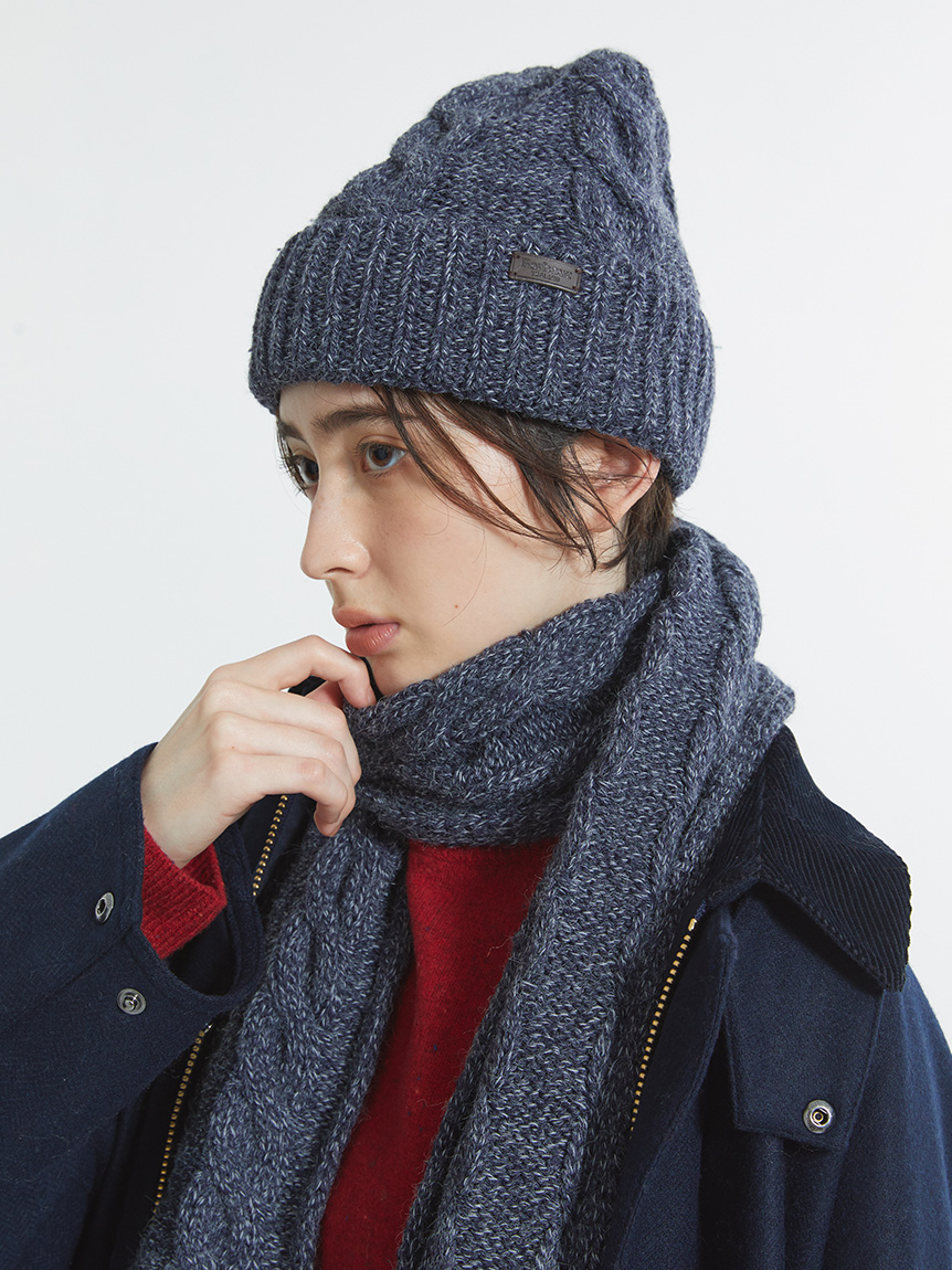 Close-up of a navy coat styled with a gray chunky-knit beanie and matching scarf over a red sweater
