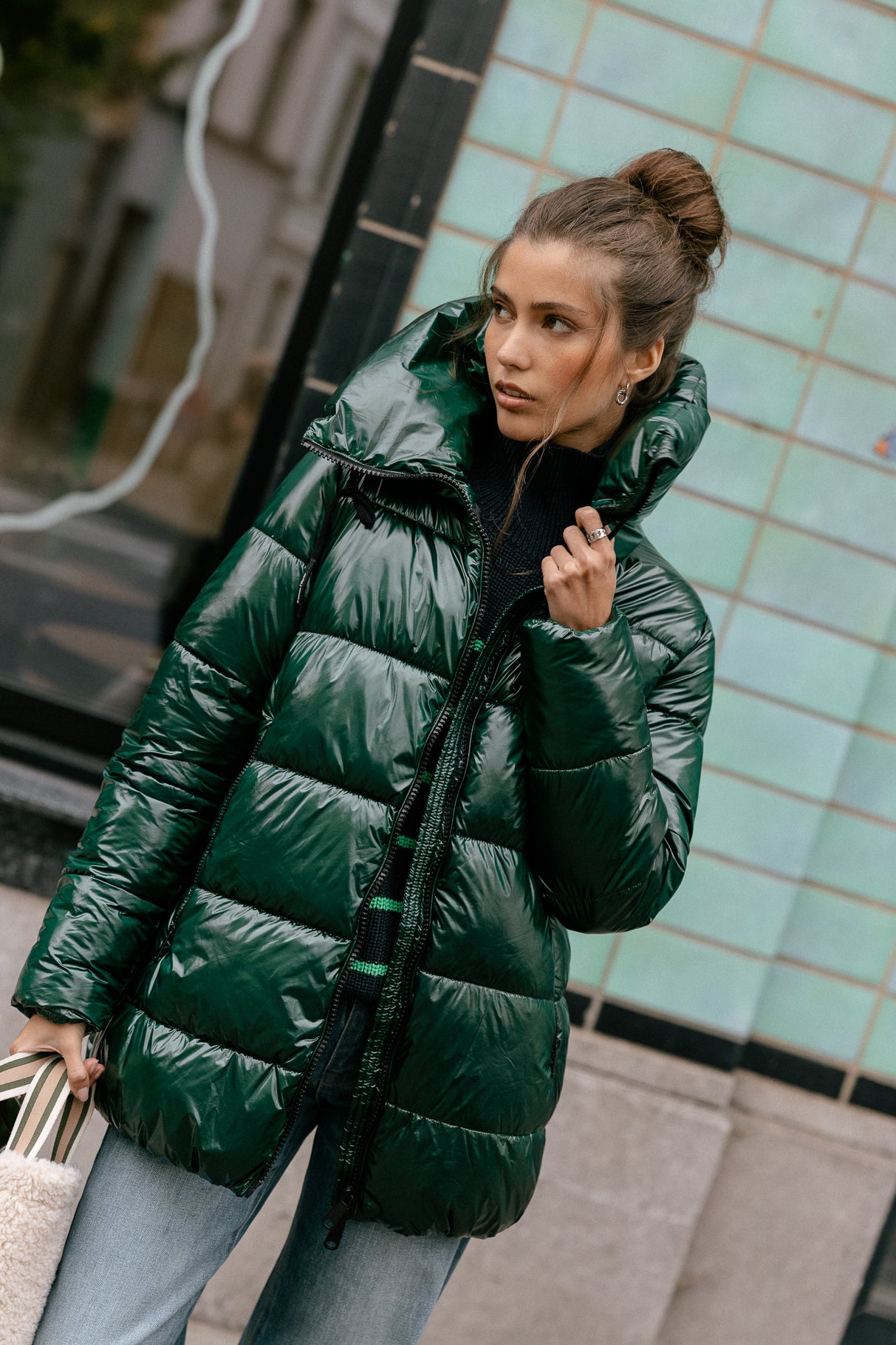 Woman wearing a glossy emerald green puffer jacket with a black turtleneck and light-wash jeans
