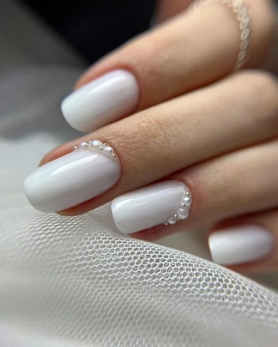 Short ivory nails with pearl accents along the cuticles