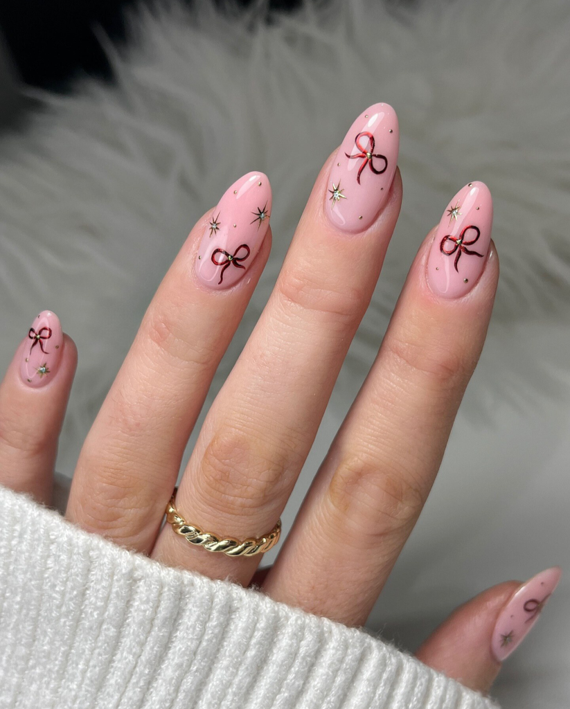 Medium almond soft pink nails with cherry red hand-painted bows and gold starburst accents