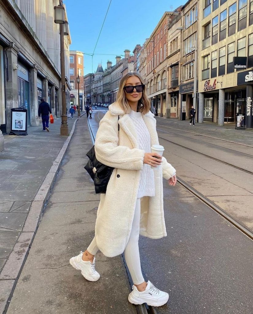 Woman wearing an all-cream outfit with a teddy coat, white sweater, white leggings and white sneakers
