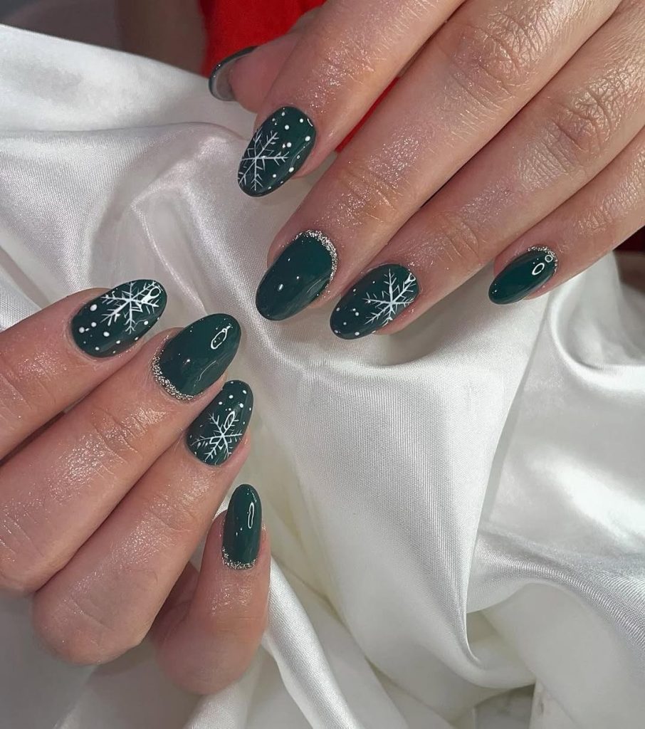 Medium almond nails in deep emerald green with white snowflake accent nail art