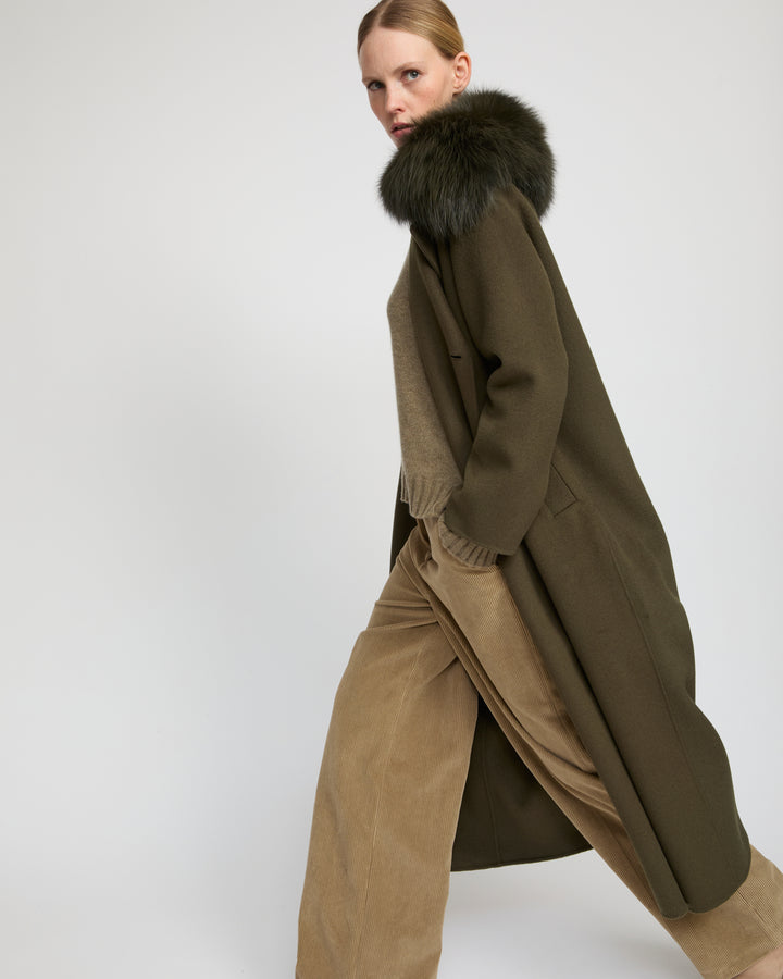 Woman in an olive wool coat with a fur collar, olive knit and tan corduroy wide-leg trousers