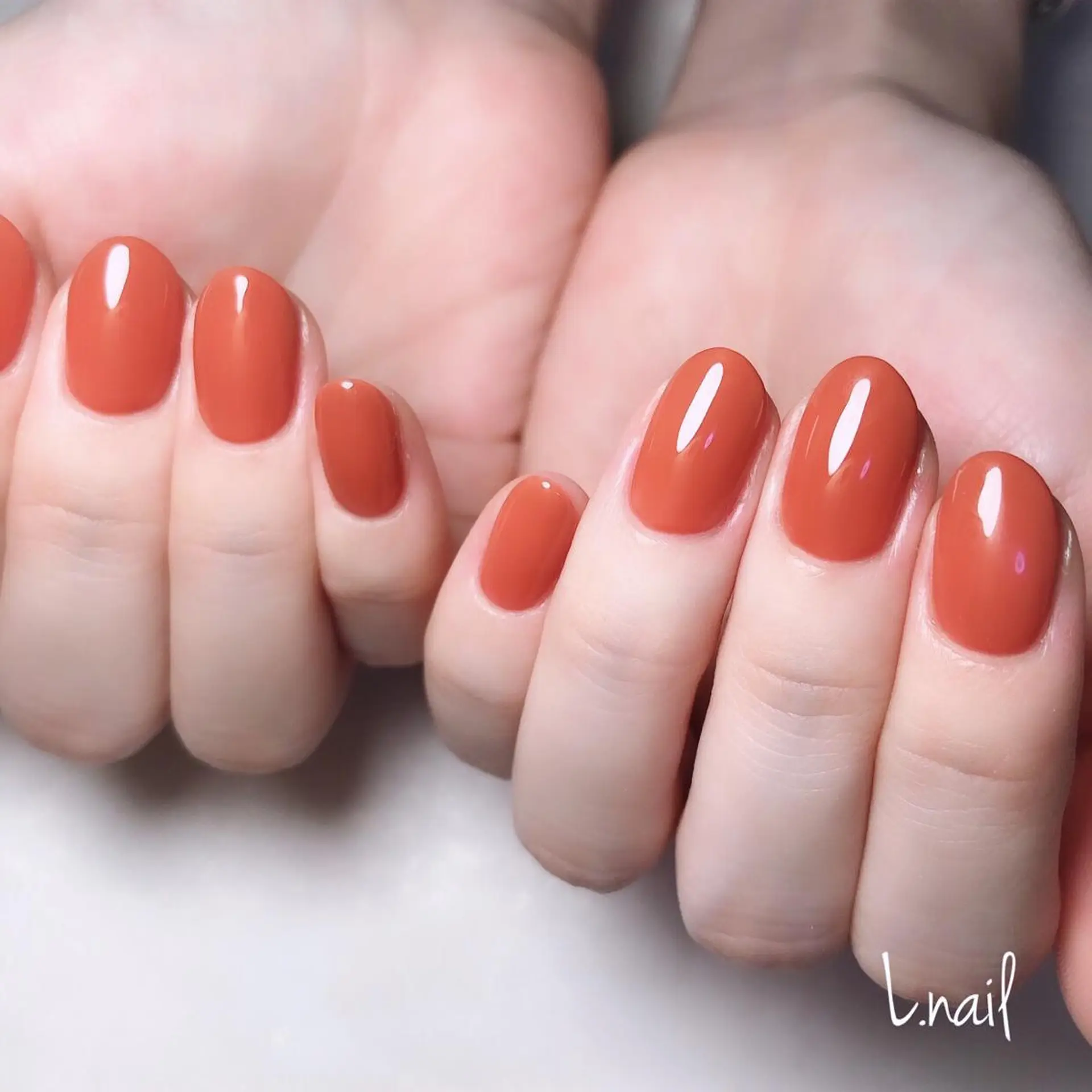 Short glossy nails in a warm terracotta red shade