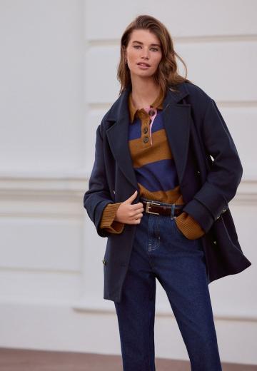 Woman in a navy oversized wool coat with a mustard and navy striped polo sweater and dark jeans