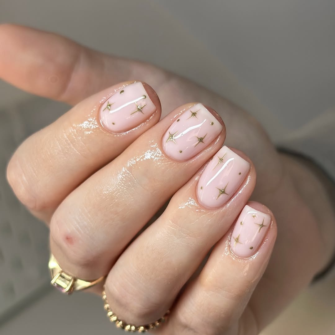 Short square milky pink nails with tiny gold star and dot accents