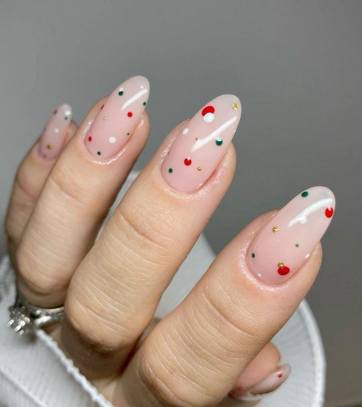 Almond nails on a sheer nude base with scattered minimal red, green, white and gold dots.