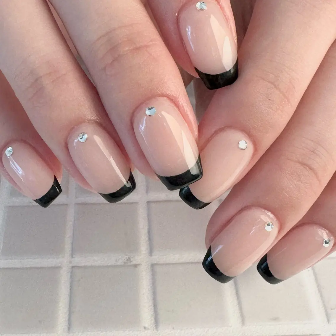 Nude nails with black French tips and a single small crystal near each cuticle