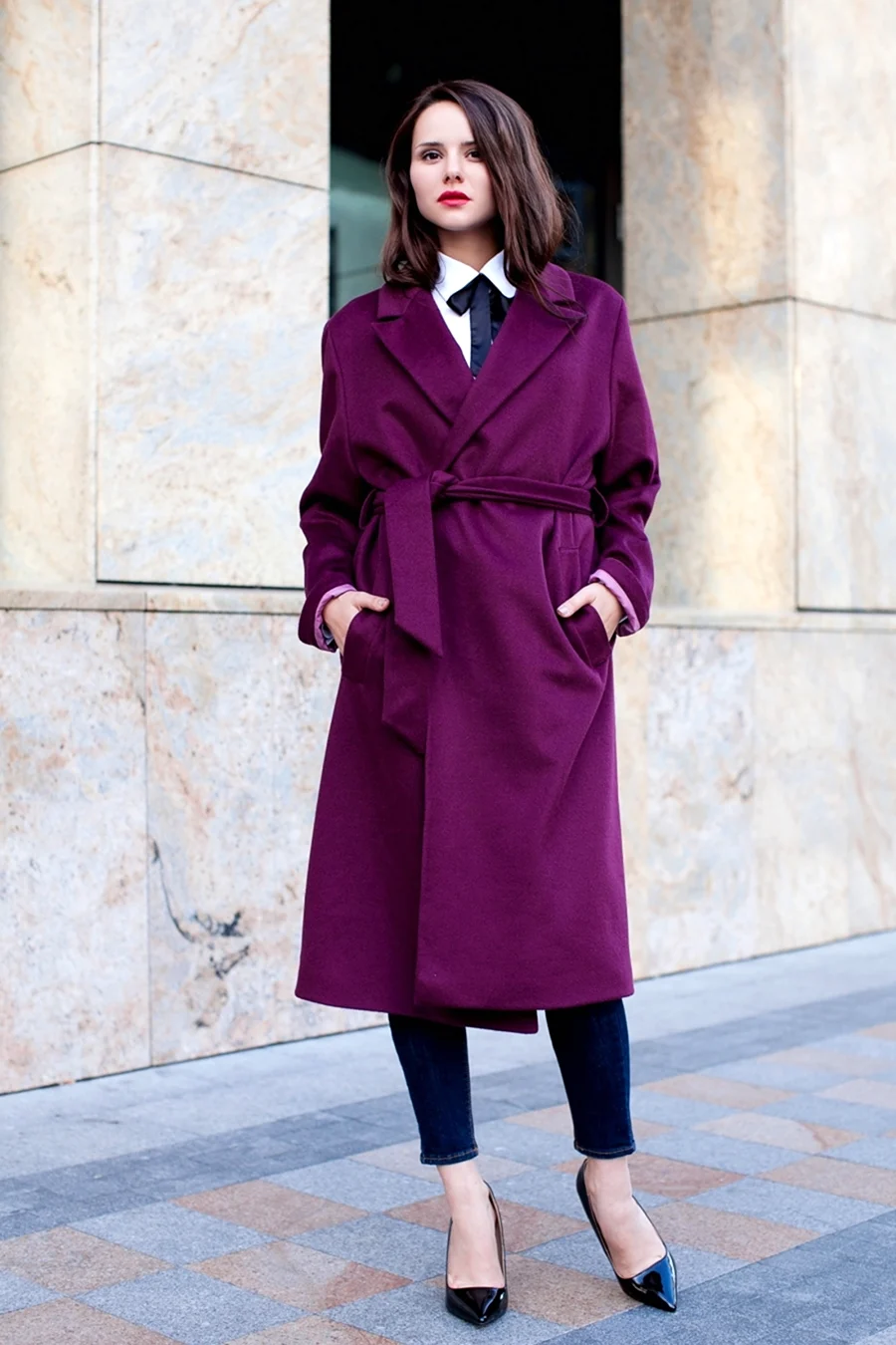 Woman in a deep plum belted wool coat with white shirt, dark tie and black pumps