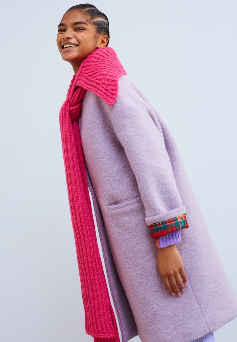 Woman in a lavender brushed wool coat with a hot pink knit scarf