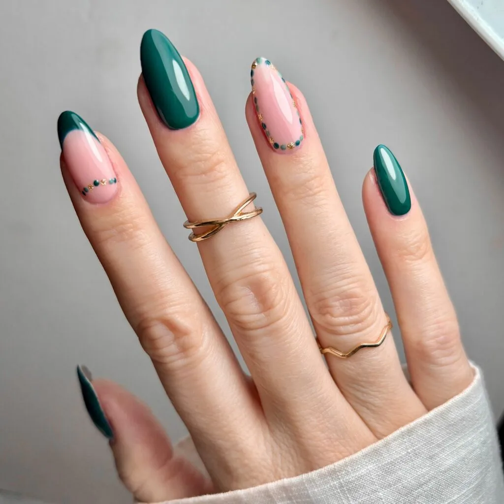 Almond nails in glossy emerald green with nude-pink accent nails with green French tips and tiny gold and green dot detailing; real photography.