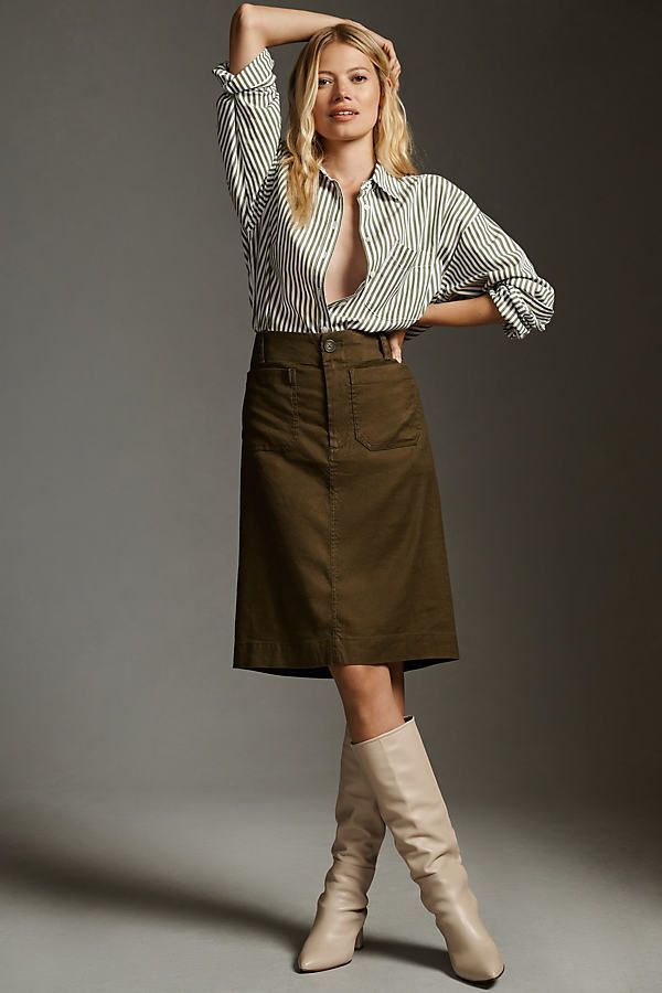 Woman in a studio wearing a green and white striped shirt, an olive midi skirt and cream knee-high boots
