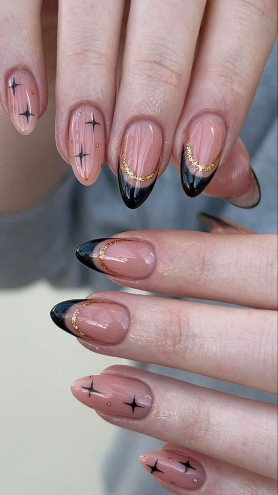 Nude almond gel nails with black French tips, gold glitter smile line and black starburst art
