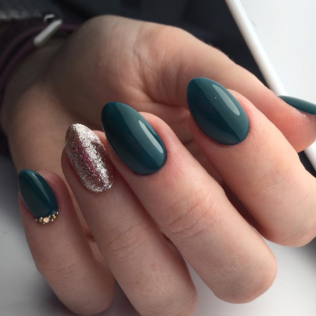 Deep teal almond nails with a silver glitter accent nail and crystal details