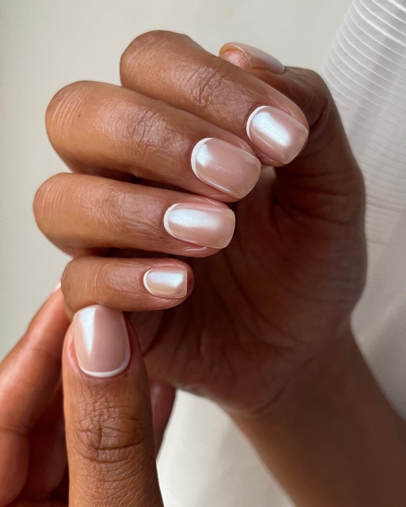 Sheer nude short nails with thin white micro French tips and a pearl shimmer finish