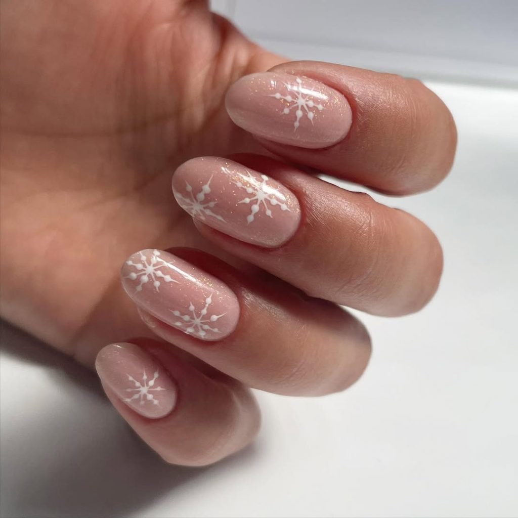 Sheer pale-pink nails decorated with delicate thin white snowflake line drawings.