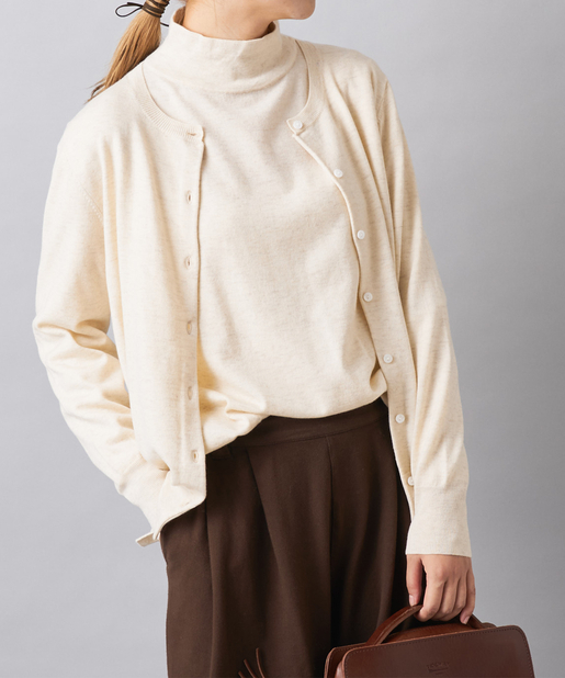 Woman layering a cream turtleneck under an open cream cardigan with brown trousers